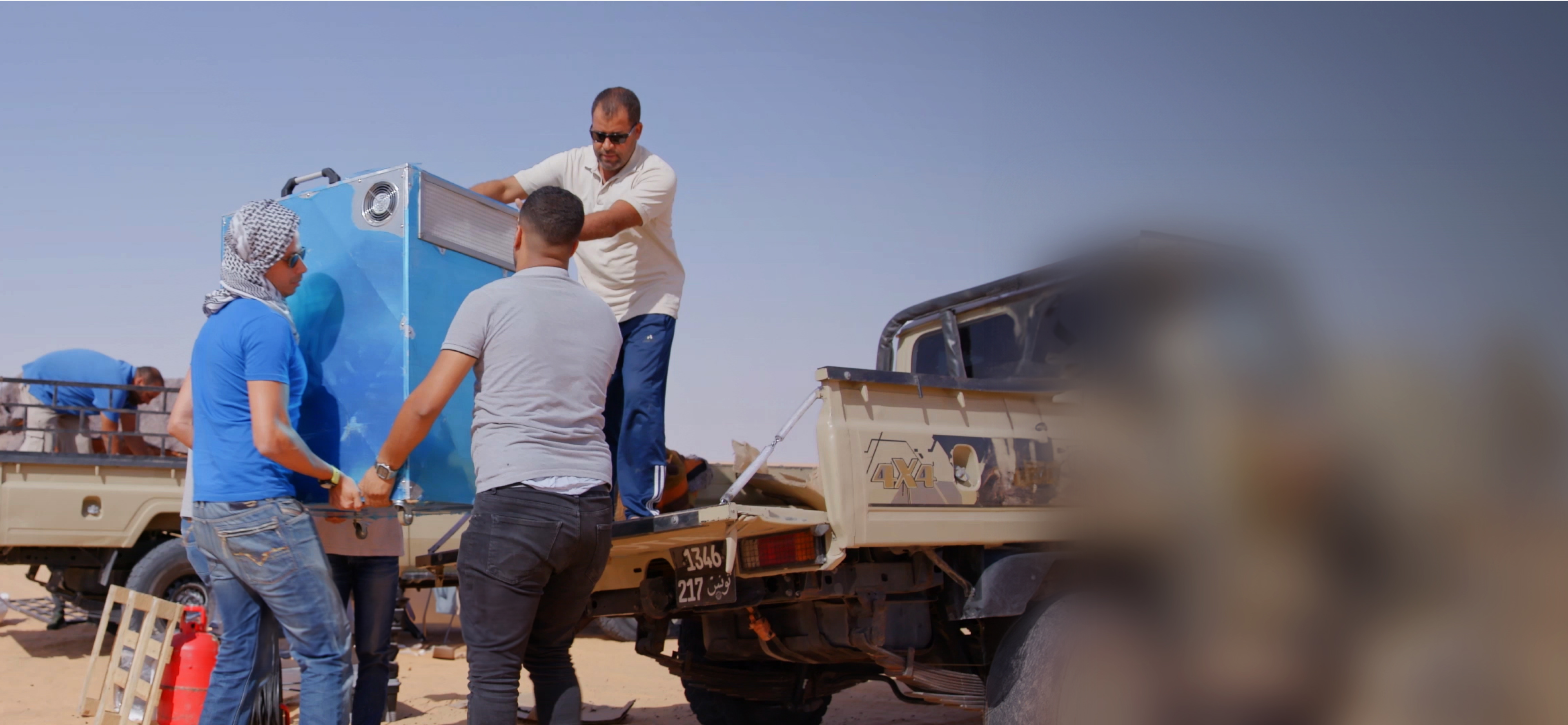 Men unloading machinery for water treatement of the back of pick up truck.