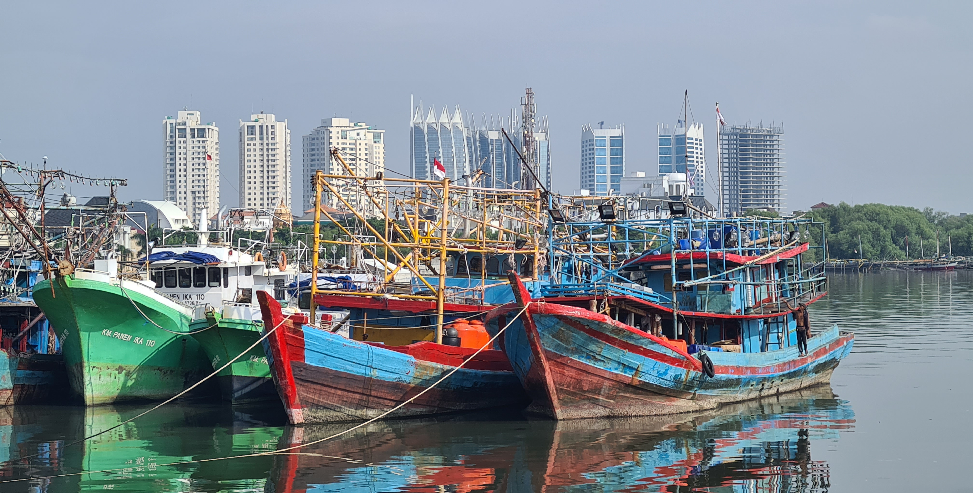 Indonesian fisher boats with modern high-rise buildings in the distance