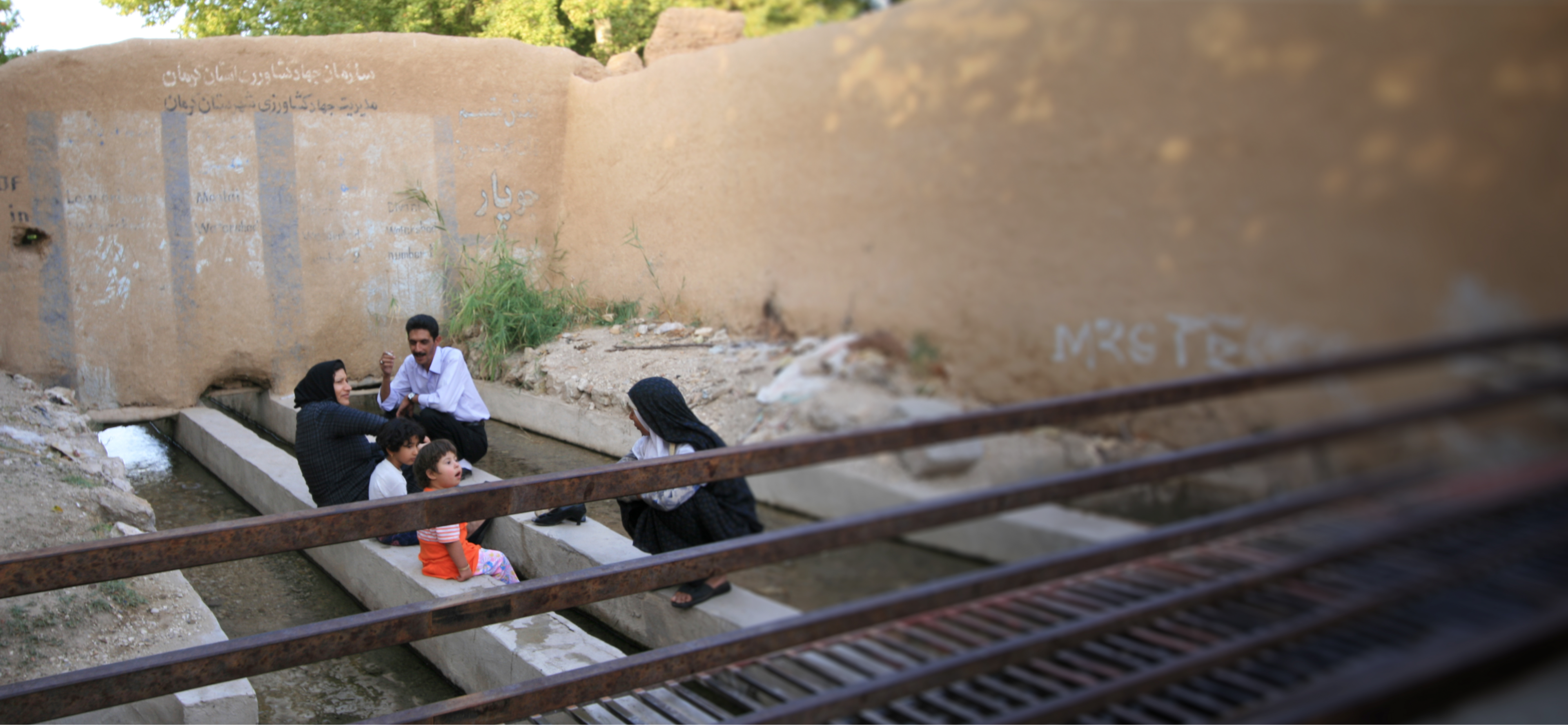A family sitting by a canal filled with fresh water from a Qanat